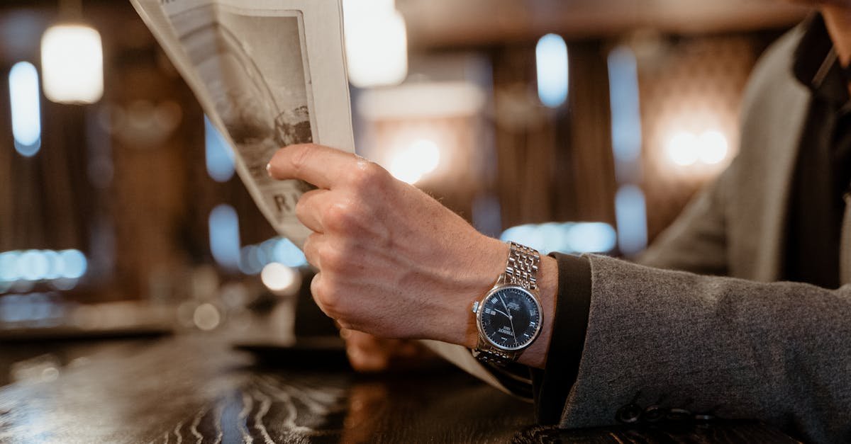 Close-up of a person's hand reading a newspaper in a cozy cafe, showcasing a classic wristwatch.